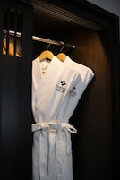 A white robe with "HOTEL du Lac" logo hanging on a wooden hanger.