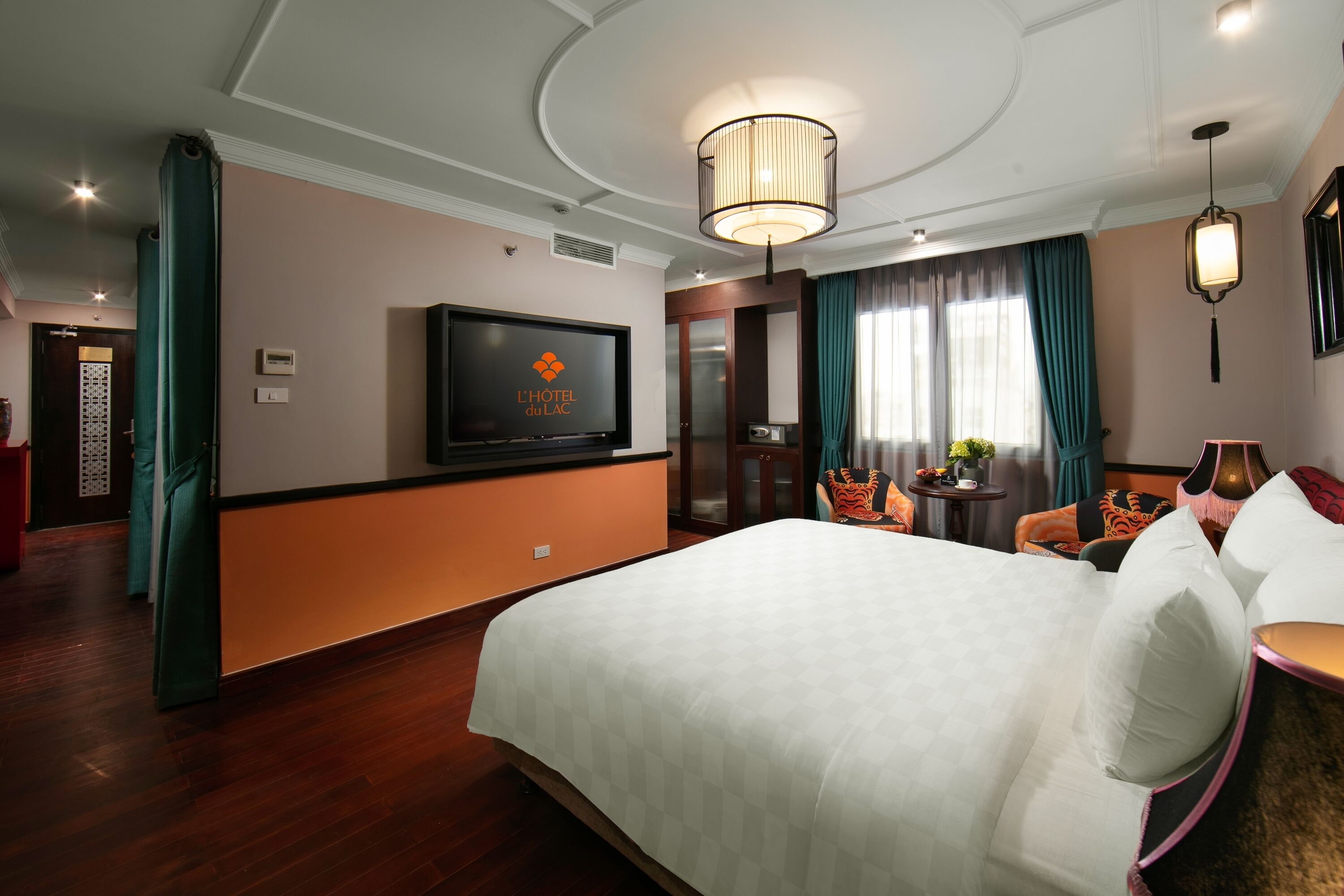 Een hotelkamer met een groot bed, een televisie aan de muur, een kroonluchter en uitzicht op het omliggende landschap.