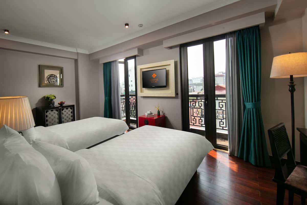 A hotel room with two beds, a TV, a desk, a lamp, and a view of the city through large windows.