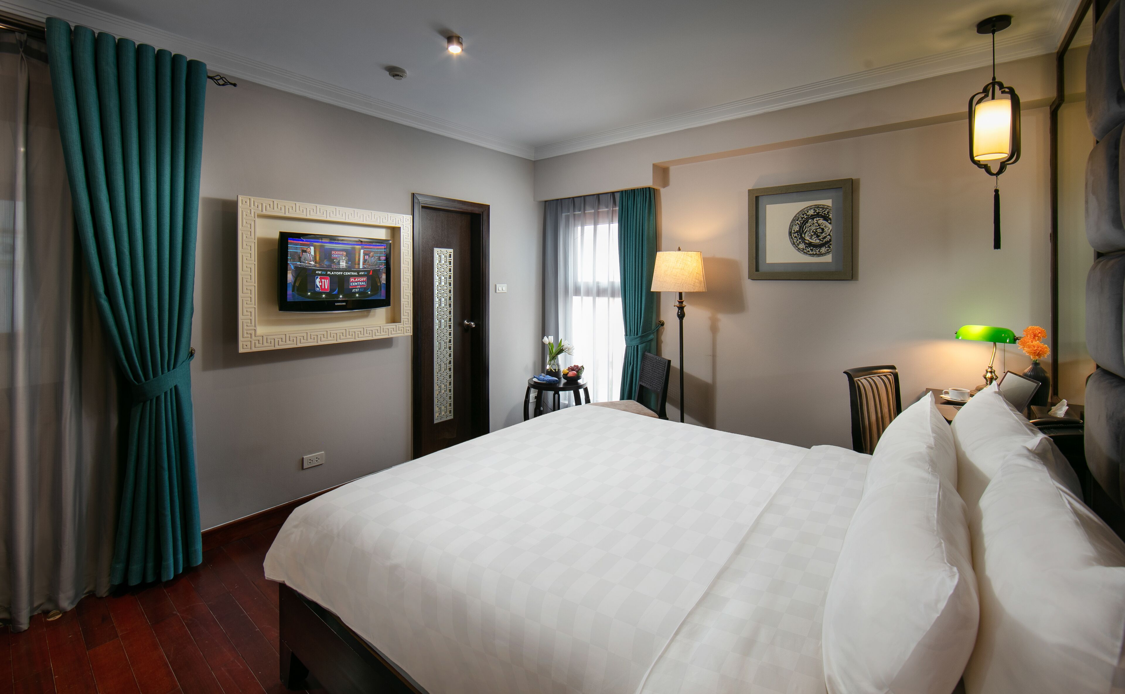 Habitación de hotel con una cama grande, un televisor montado en la pared, un escritorio con lámpara y un cuadro enmarcado en la pared.