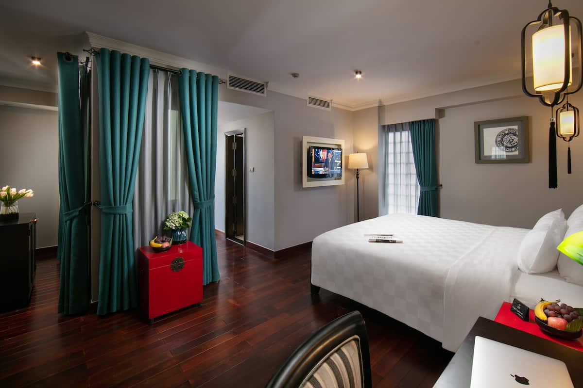 A hotel room with a bed, a desk, a chair, a TV, and a lamp.