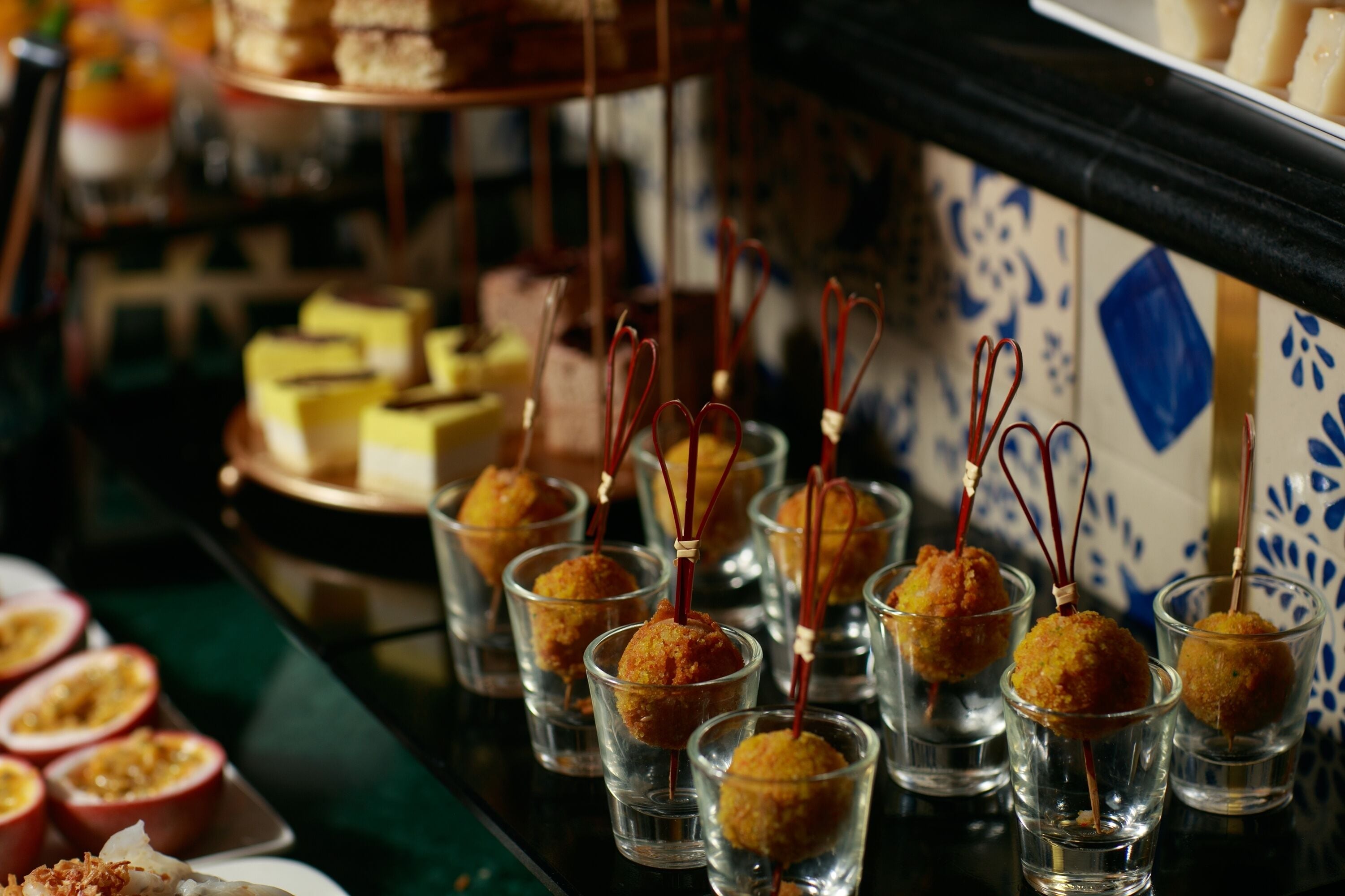A selection of food items, including small cups with golden-brown balls and skewers, and a variety of other dishes on a table.