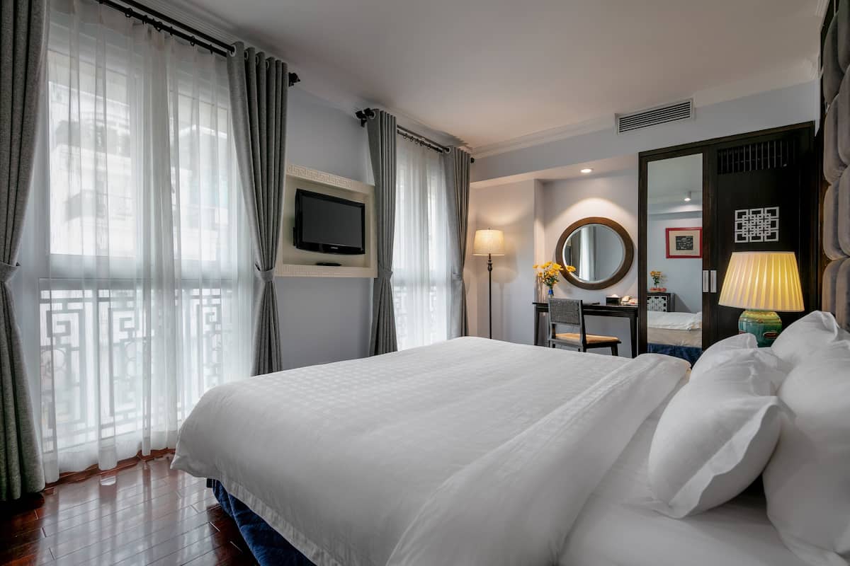 A hotel room with a large bed, a TV, a desk with a lamp, and a mirror.