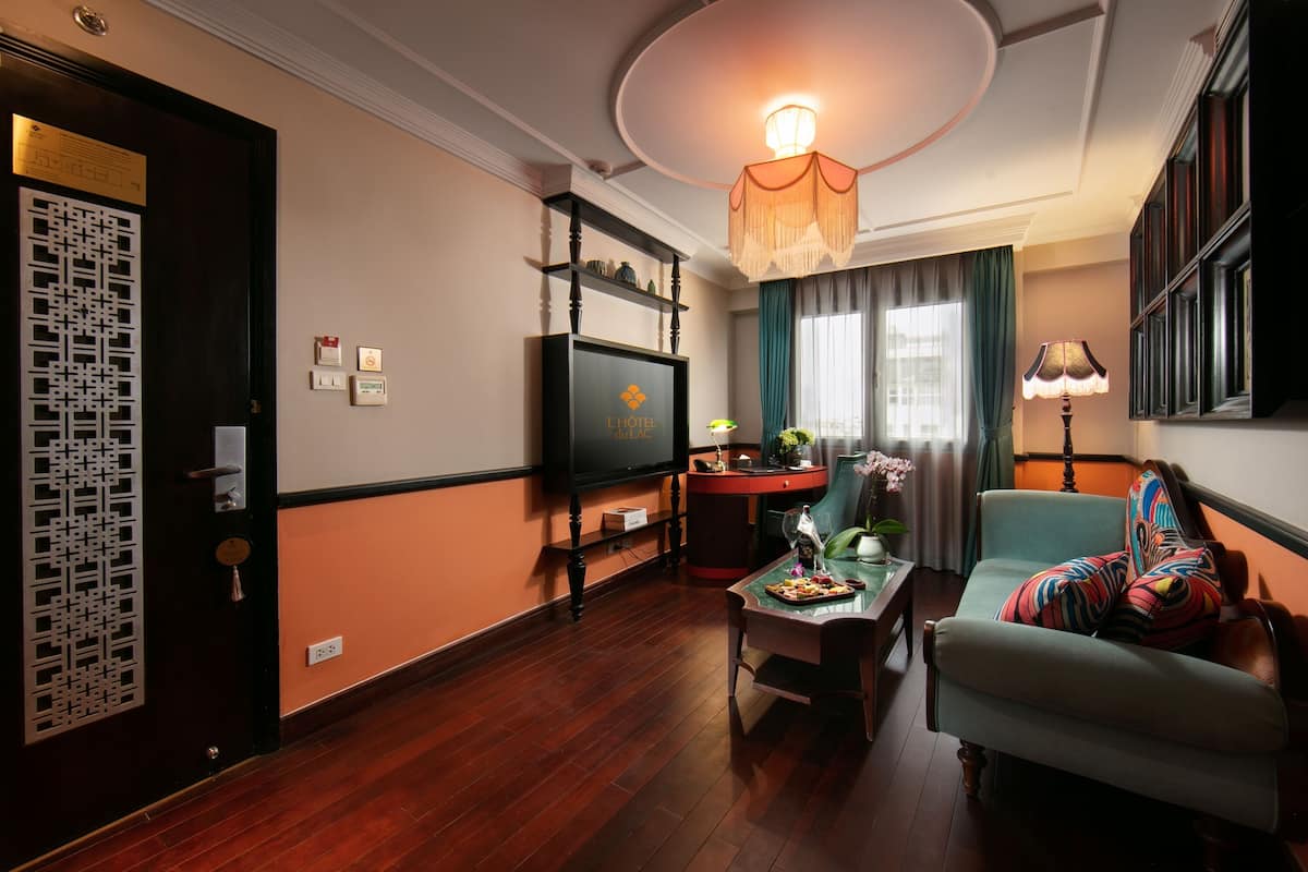 A hotel room with a wooden floor, a television, a sofa, a coffee table, and a chandelier.