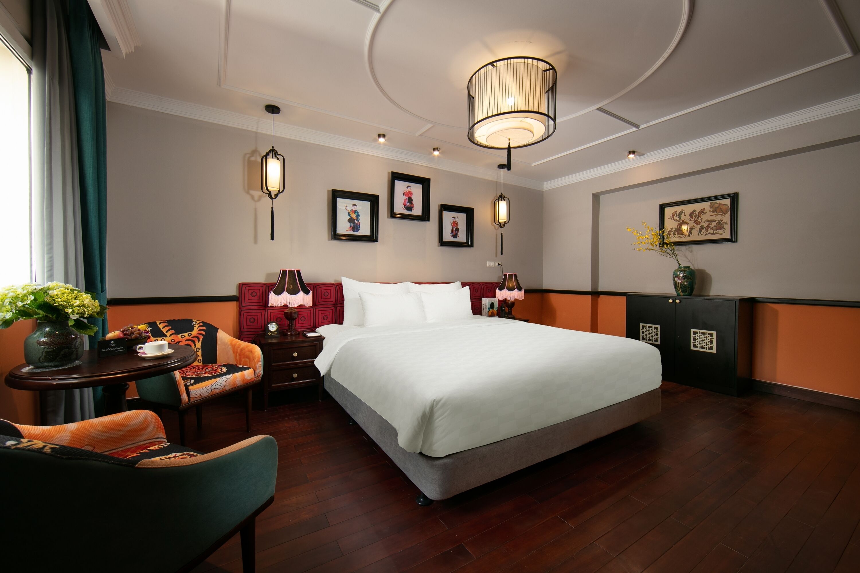 A hotel room with a large bed, a desk with a chair, a vase with flowers, and framed pictures on the walls.