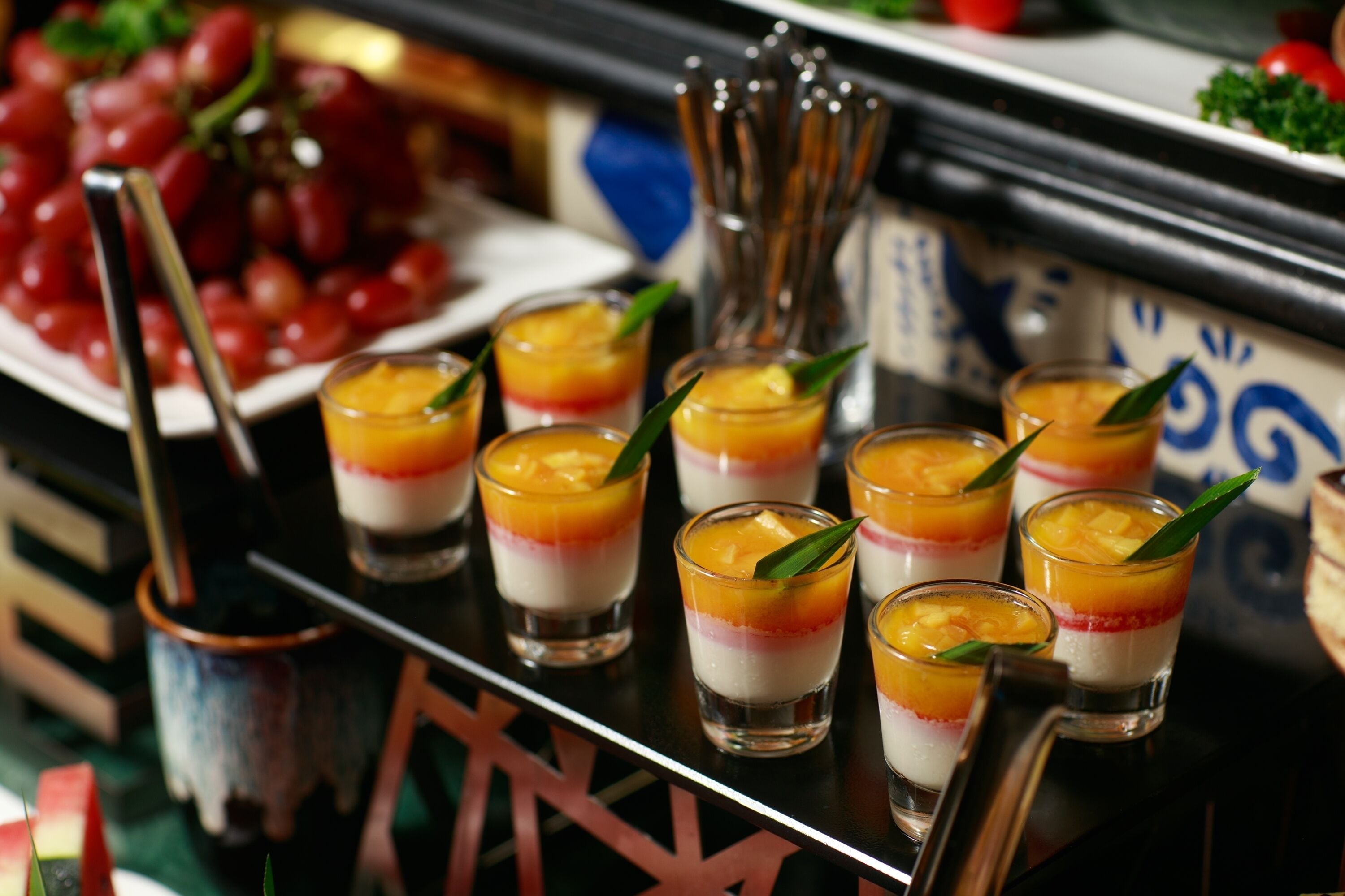 Un buffet de desserts proposant des parfaits aux fruits en couches, ainsi qu’un assortiment de fruits frais et de couverts.