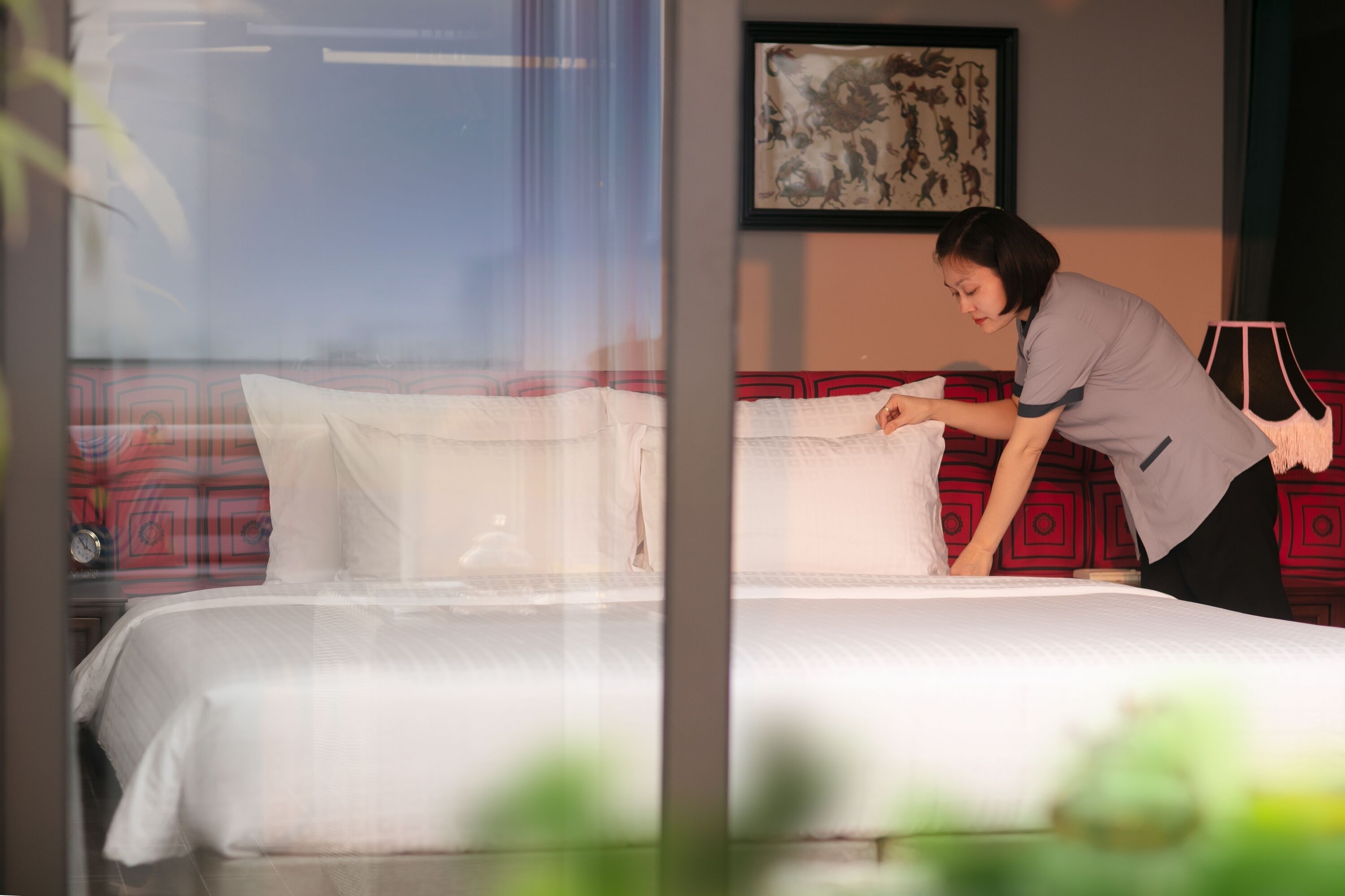 A neatly made bed with white linens, a red patterned bedspread, and a framed artwork on the wall.