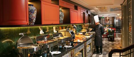 Buffet-alue, jossa kokki valmistaa ruokaa, punaiset kaapit ja laatoitettu seinäpinta.
