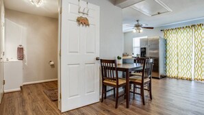 A room with a wooden floor, a white door, a dining table with chairs, a ceiling fan, and a kitchen area with a refrigerator and a window. - prof cleaned*Peaceful & Close 2 Dwntwn (Dallas)
