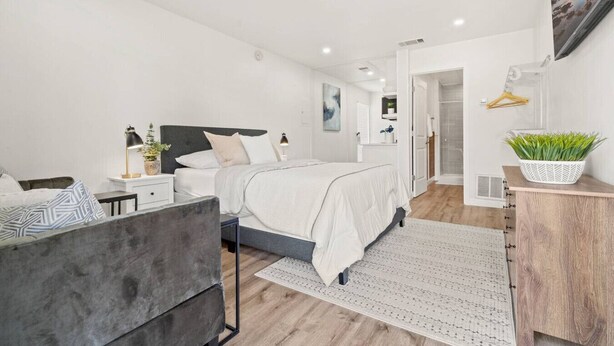 A modern bedroom with a bed, bedside tables, a desk, a chair, a plant, and a shower area. - Month Discount!Quiet Studio Apartment*Walk to UTA* (Arlington)