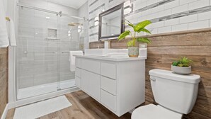 A modern bathroom with a glass shower enclosure, white cabinetry, and a wooden accent wall. - Month Discount!Quiet Studio Apartment*Walk to UTA* (Arlington)
