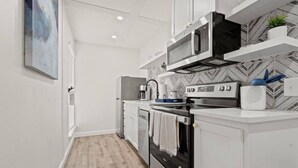 A modern kitchen with white cabinetry, a microwave, a coffee maker, and a patterned backsplash.