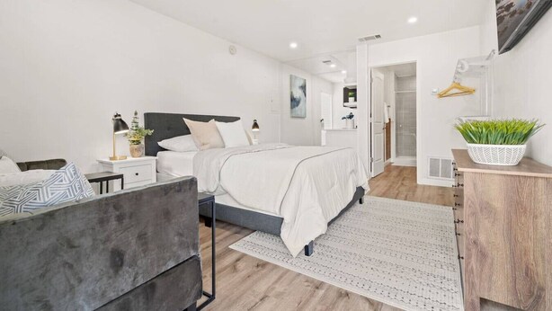 A modern bedroom with a bed, bedside tables, a desk, and a shower area.