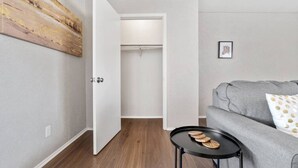 A room with a grey sofa, a small round table with wooden coasters, a closet with a white door, and a painting on the wall.
