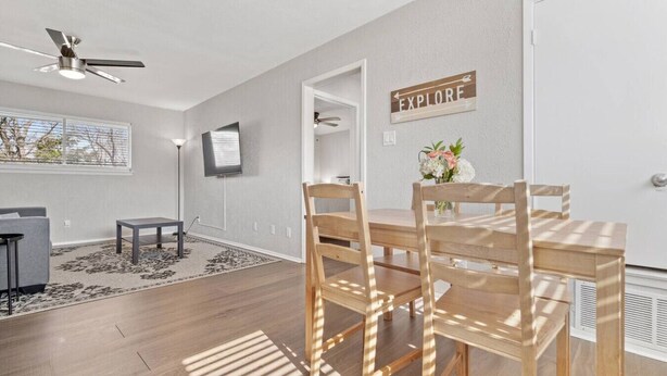 A modern living room with a dining area, a ceiling fan, a flat-screen TV, and a sign that says 'EXPLORE'.
