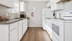 A compact kitchen with white cabinets, a microwave, a stove, and a fire extinguisher.