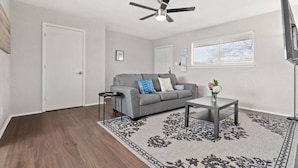 A living room with a grey sofa, a coffee table, a patterned rug, a ceiling fan, and a TV.