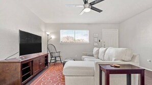 A living room with a TV, a ceiling fan, a window, a sofa, and a small table. - Walk to AT&T! Family-Friendly 2 Queen Beds (Arlington)