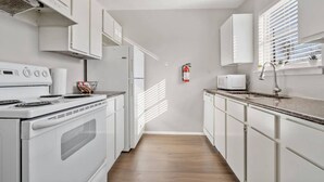 A narrow kitchen with white cabinets, a stove, a microwave, and a window with blinds. - Walk to AT&T! Family-Friendly 2 Queen Beds (Arlington)
