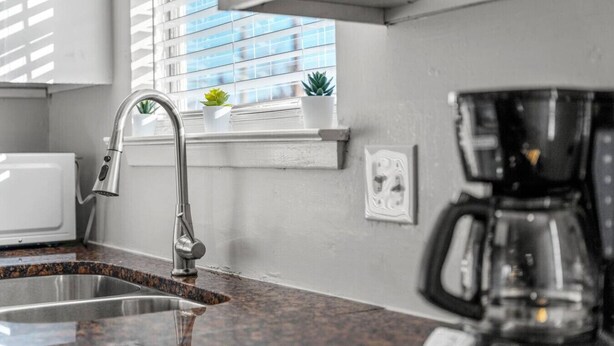 A kitchen with a stainless steel sink, a coffee maker, and a window with blinds. - Walk to AT&T! Family-Friendly 2 Queen Beds (Arlington)