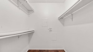 Una habitació petita i buida amb parets blanques, un terra de fusta i dues prestatgeries blanques.