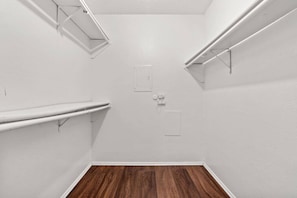 Una habitación pequeña y vacía, con paredes blancas, suelo de madera y dos estantes blancos.