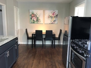 Uma cozinha com mesa de jantar, cadeiras, geladeira e fogão.