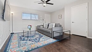 A living room with a gray sofa, a coffee table, a patterned rug, a ceiling fan, and a door. - World Cup Walkable | King Bed Retreat (Arlington)