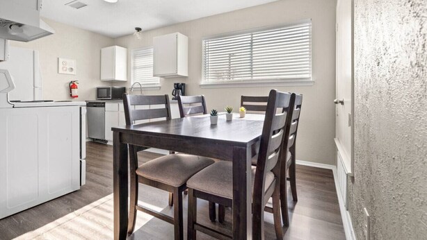 A modern kitchen with white cabinets, a dining table with chairs, and a window with blinds. - World Cup Walkable | King Bed Retreat (Arlington)