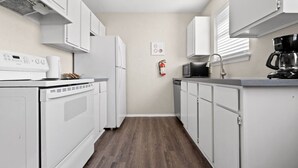 A compact kitchen with white appliances, a microwave, a coffee maker, and a fire extinguisher on the wall. - World Cup Walkable | King Bed Retreat (Arlington)