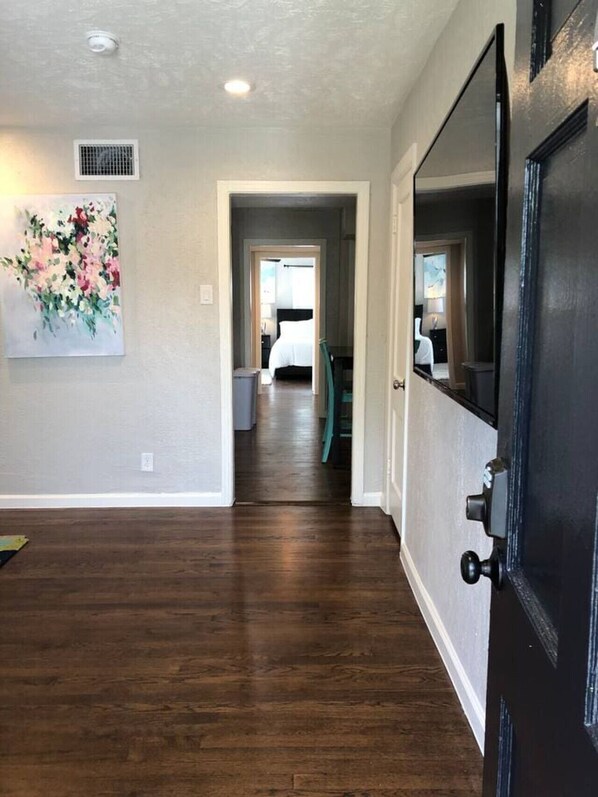 A hallway with hardwood flooring, a door with a black handle, and a painting on the wall.
