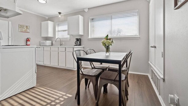 A modern kitchen with white cabinets, a dining table with chairs, and a window with blinds.