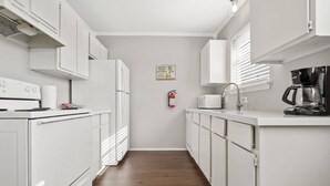 A narrow kitchen with white cabinets, a microwave, a coffee maker, and a fire extinguisher on the wall.