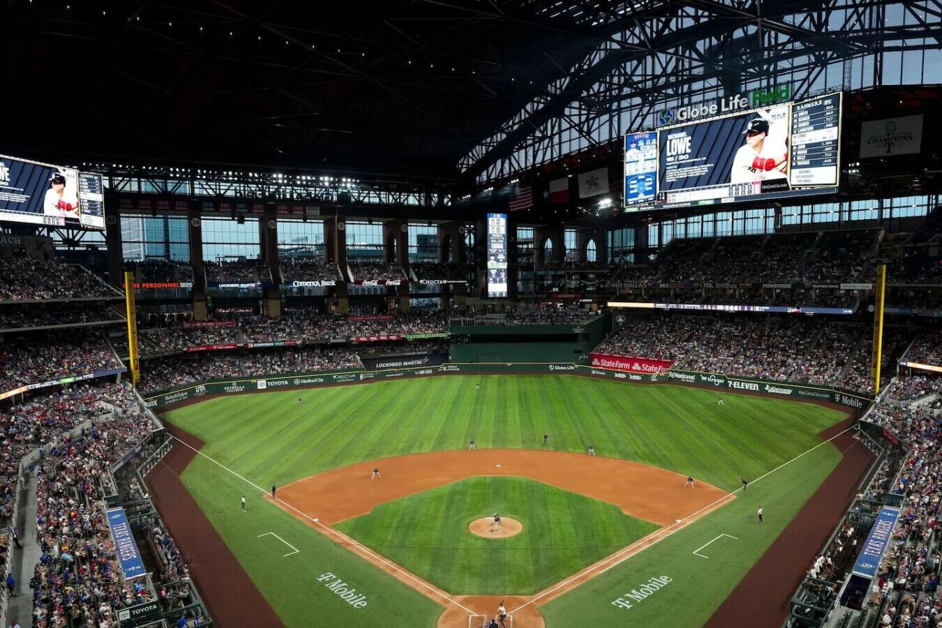 A large stadium with multiple tiers of seating, a central field, and large digital displays.