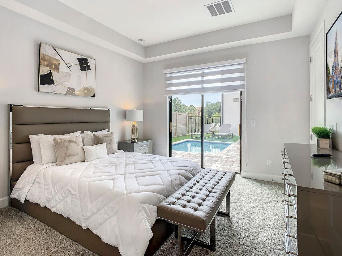 Une chambre moderne avec un grand lit, un banc, un bureau et une vue sur une piscine.
