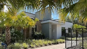 Una casa moderna con entrada pavimentada, palmeras y un portón metálico.