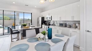 Una cocina moderna con armarios blancos, una isla central y un comedor con mesa y sillas.