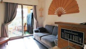 Een woonkamer met een grijze bank, een ventilator en een bord met de tekst 'Guadeloupe TI KAZ ARHUM'.