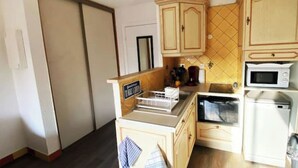 Een kleine keuken met houten kastjes, een magnetron en een koffiezetapparaat.