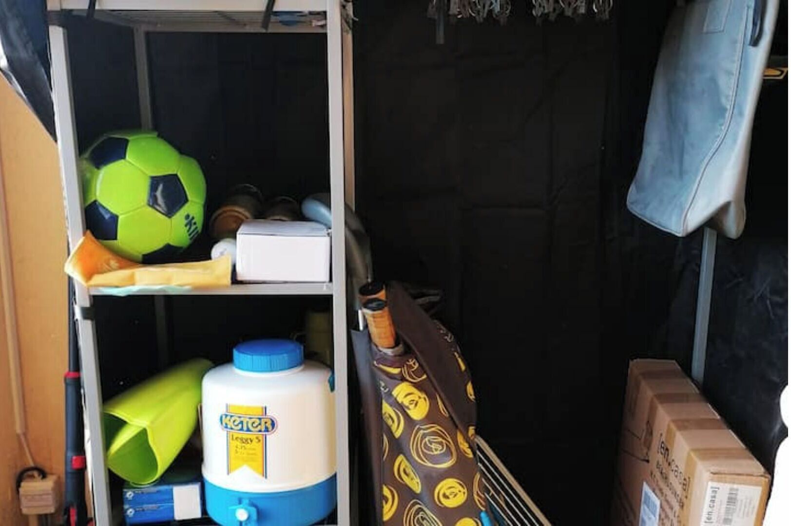 Ett förvaringsutrymme med en fotboll, en stor vattenbehållare och en mönstrad väska.