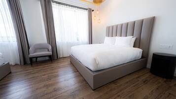 A modern hotel room with a large bed, a chair, a bedside table, and a window with curtains.