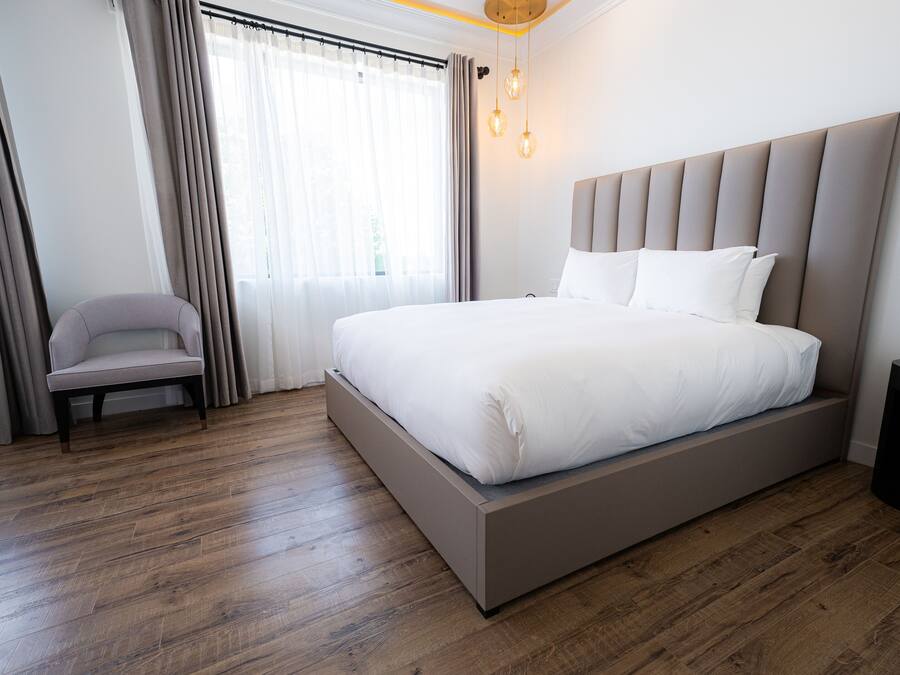A modern hotel room with a large bed, a chair, a bedside table, and a window with curtains.