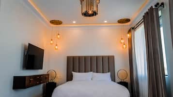 A modern hotel room with a large bed, a flat-screen TV, and a chandelier.