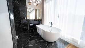 A modern bathroom with a freestanding bathtub, a vanity with a mirror, and a large window with sheer curtains. - Mount Alverno Luxury Resorts (Caledon)