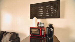 A room with a black coffee maker, a red microwave, and a black coffee pot on a reflective surface. A sign above reads "WE HOPE YOU ENJOYED OUR STAY. PLEASE DON'T FORGET TO LEAVE YOUR PARKING PASS & KEY FOR SAFE TRAVEL."