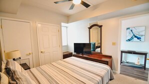 A bedroom with a bed, a television, a dresser, a mirror, and a painting on the wall.