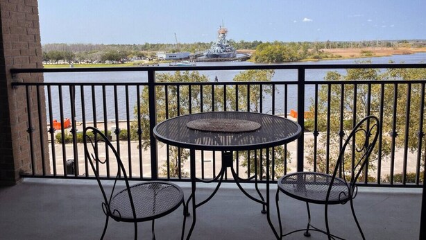 A balcony with a table and chairs, overlooking a body of water and a ship.