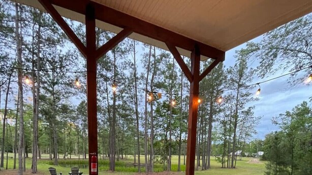 Un patio exterior con mobiliario de madera, incluyendo sofás y una mesa, bajo una pérgola de madera.