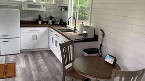 Cocina compacta con armarios blancos, microondas integrado y cafetera. Una ventana ofrece luz natural y vistas a la vegetación.