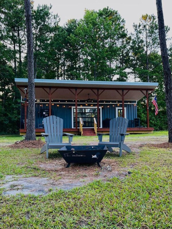 A cabin with a covered porch, two Adirondack chairs, and a fire pit. - Shipping Container Cabin Couples Paradise! (Rocky Point)
